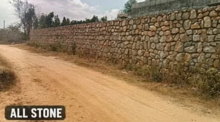 Long all-stone compound wall along dirt road