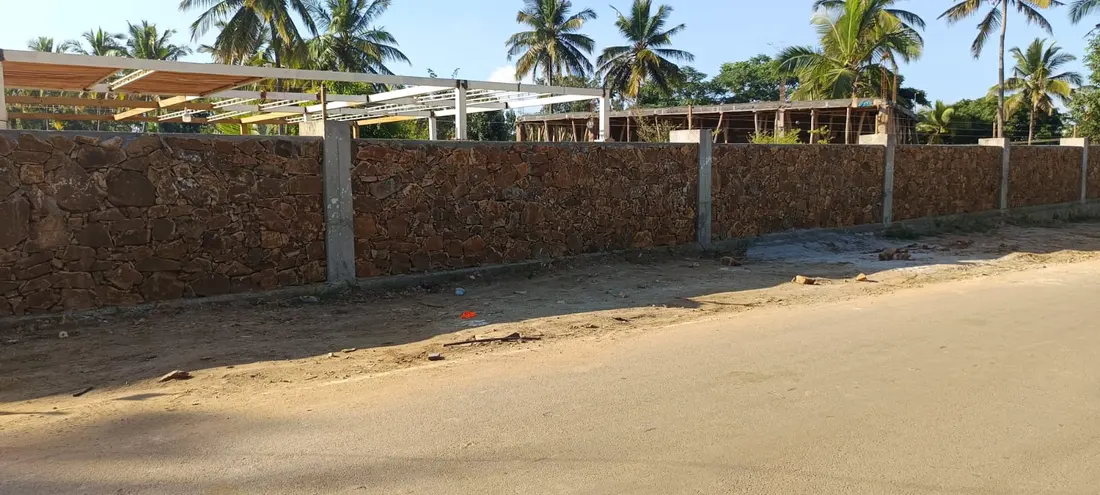Compound wall construction along roadside with palm trees